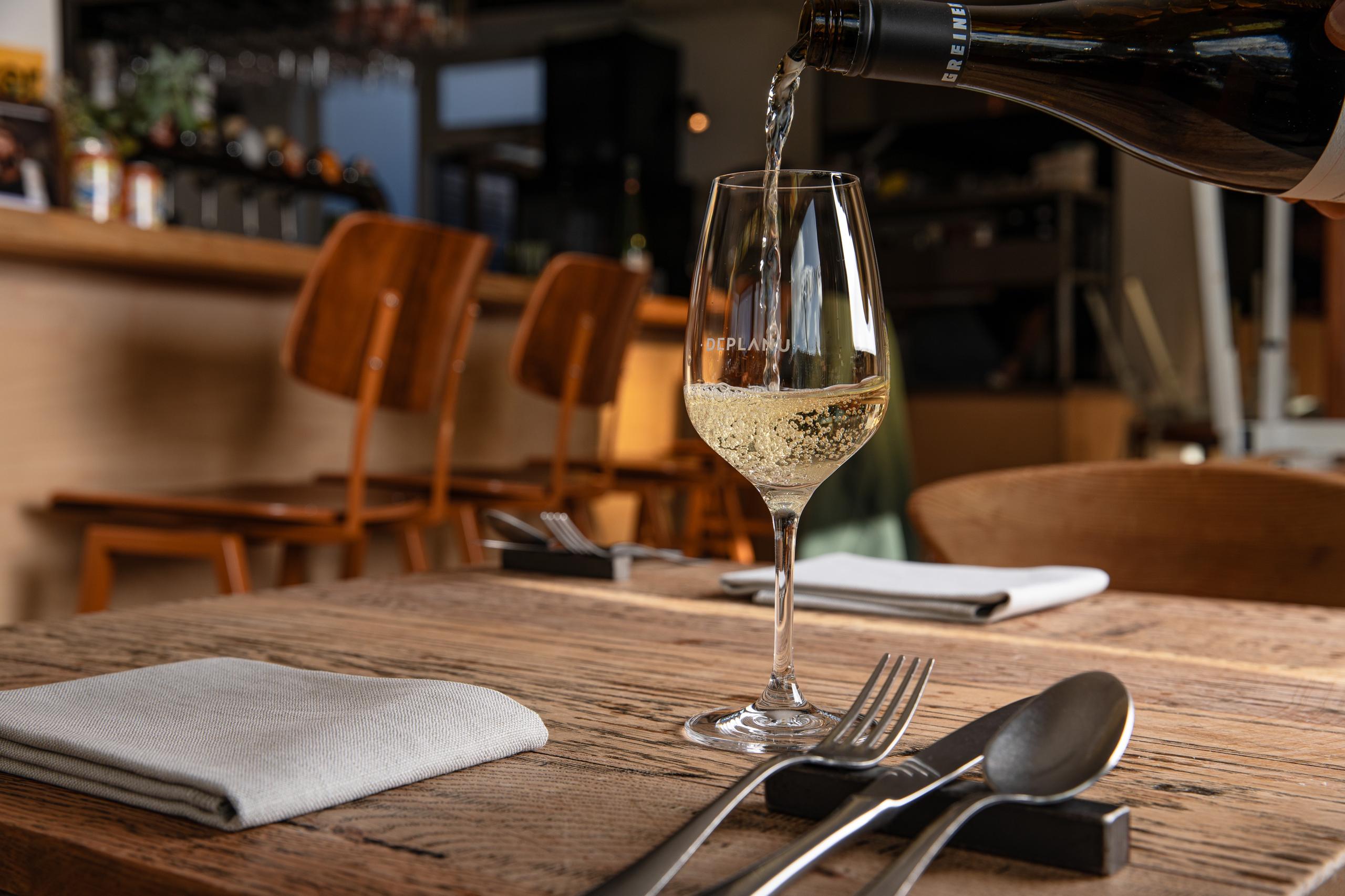 Nagerecht bij zonlicht op hout bij Deplanu, met wijn en bediening aan tafel.