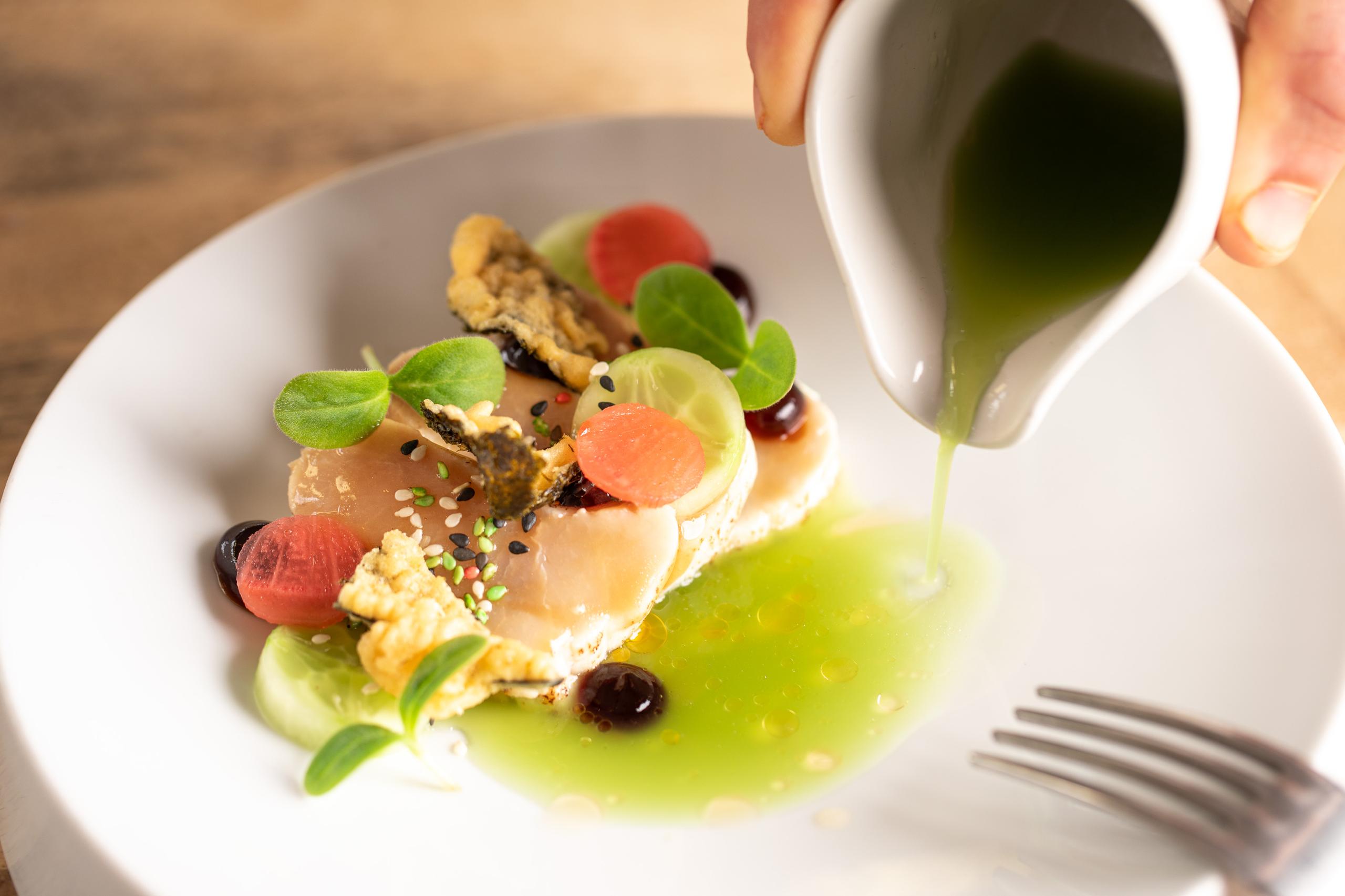 Afronden aan tafel: groene saus over een gerecht wordt geschonken in Restaurant Deplanu, Haarlem.
