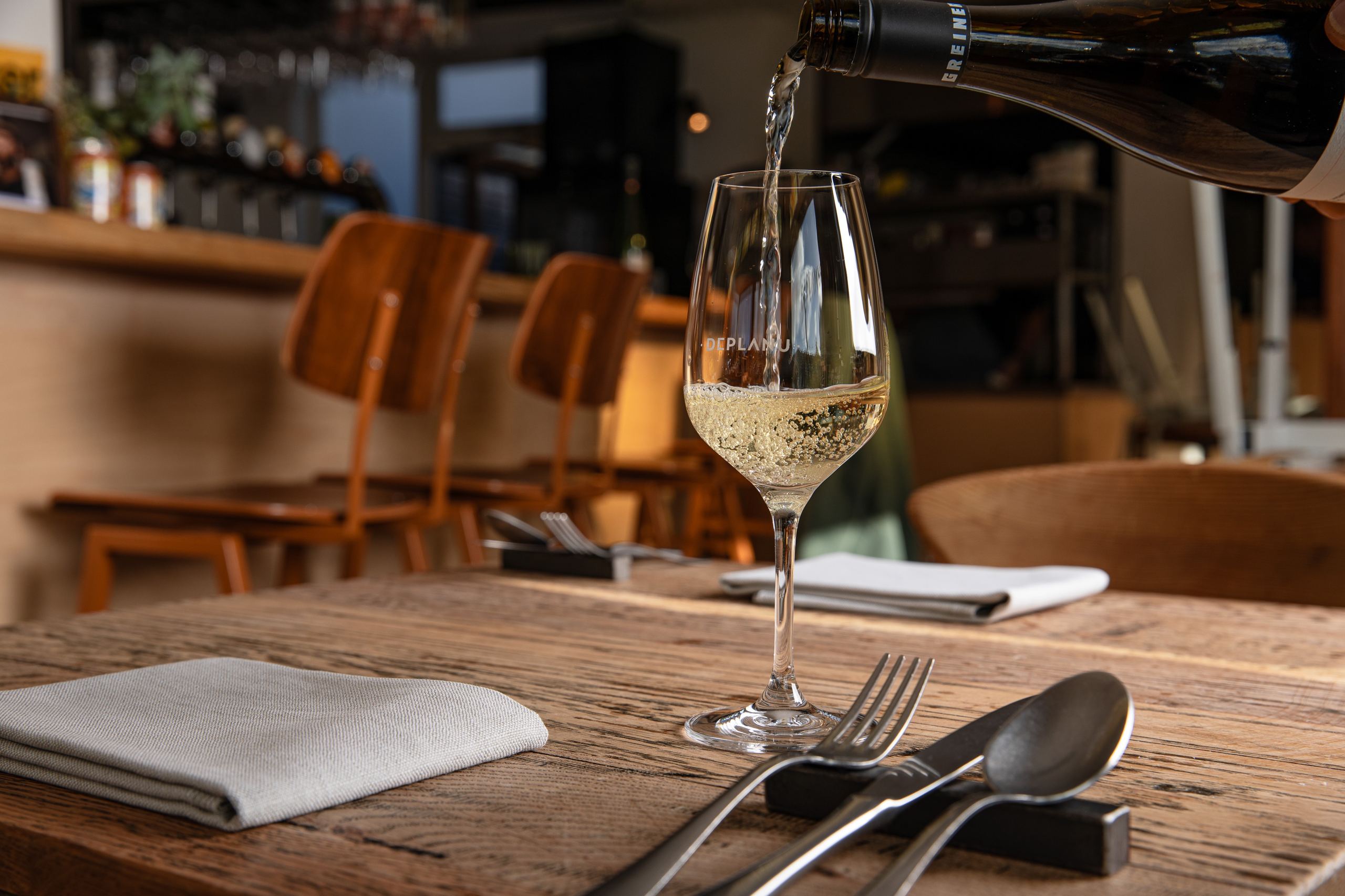 Nagerecht bij zonlicht op hout bij Deplanu, met wijn en bediening aan tafel.